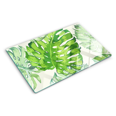 Üveg vágódeszka fényképpel Monstera levelek világos háttér előtt