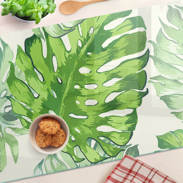 Üveg vágódeszka fényképpel Monstera levelek világos háttér előtt