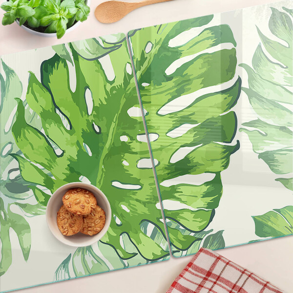 Üveg vágódeszka fényképpel Monstera levelek világos háttér előtt