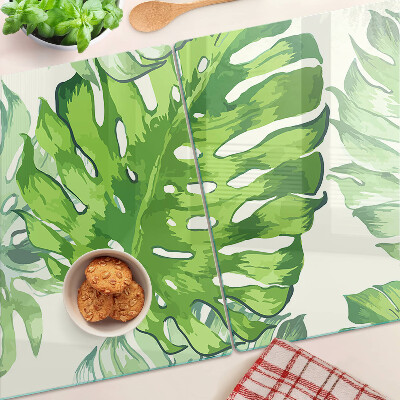 Üveg vágódeszka fényképpel Monstera levelek világos háttér előtt